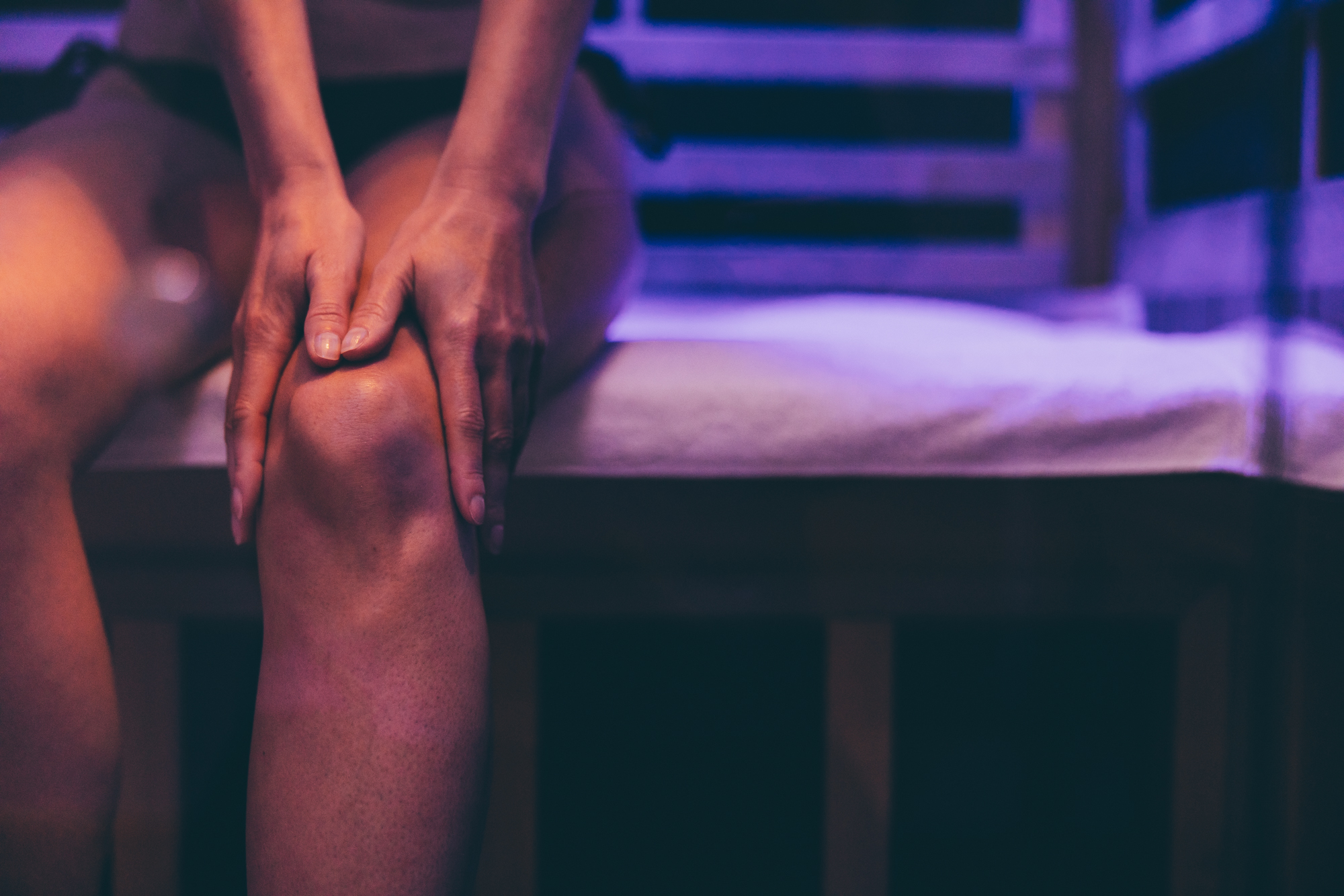 A woman sits in a sauna. She massages her leg after injury to promote recovery.